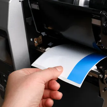 Hand applying blue custom thermal label from thermal transfer printer
