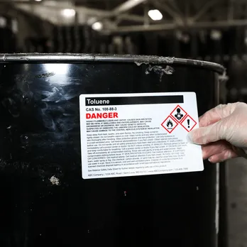Chemical drum with white digitally printed hazard warning label being applied