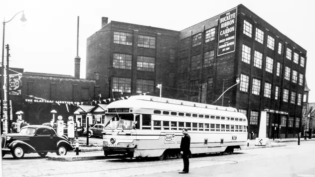 A vintage black and white photo showing a man standing in front of a street car