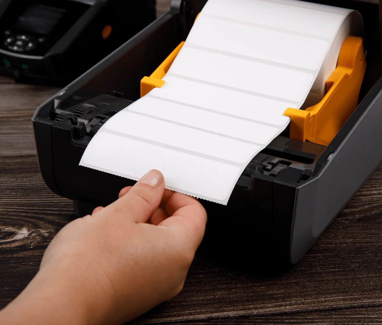 a hand pulling a roll of small blank labels through a desktop thermal label printer