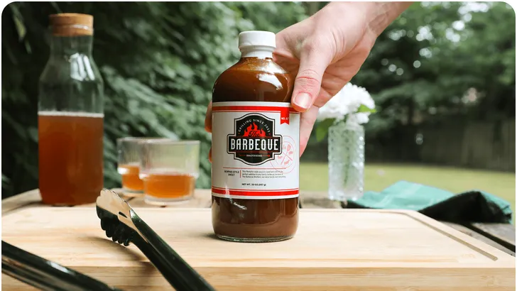 a large bottle of barbeque sauce with a printed label being sat down on a table