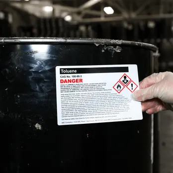 Black hazardous material container with safety warning label and diamond-shaped hazmat symbol