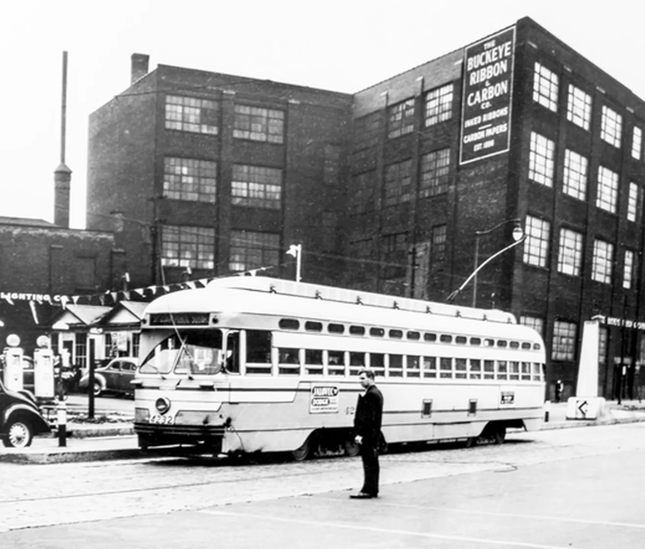 Vintage black and white photo of a streetcar and man standing in front of an industrial building