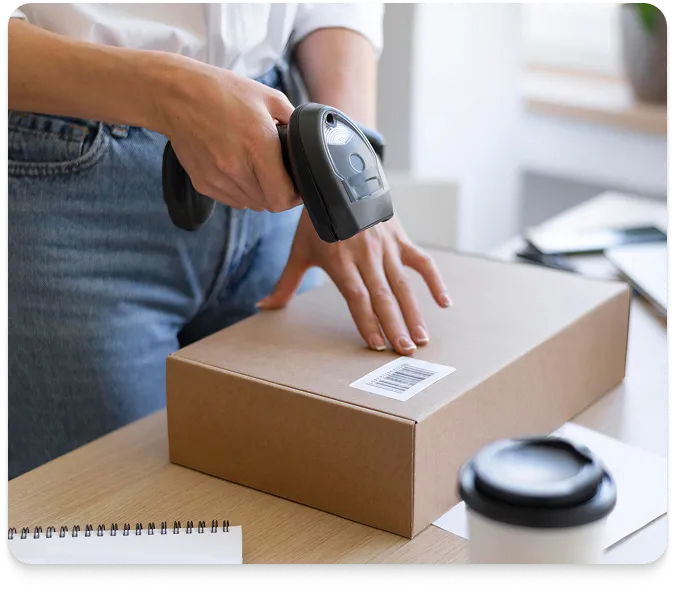 a person using a handheld barcode scanner to scan a barcode label on a rectangular cardboard box