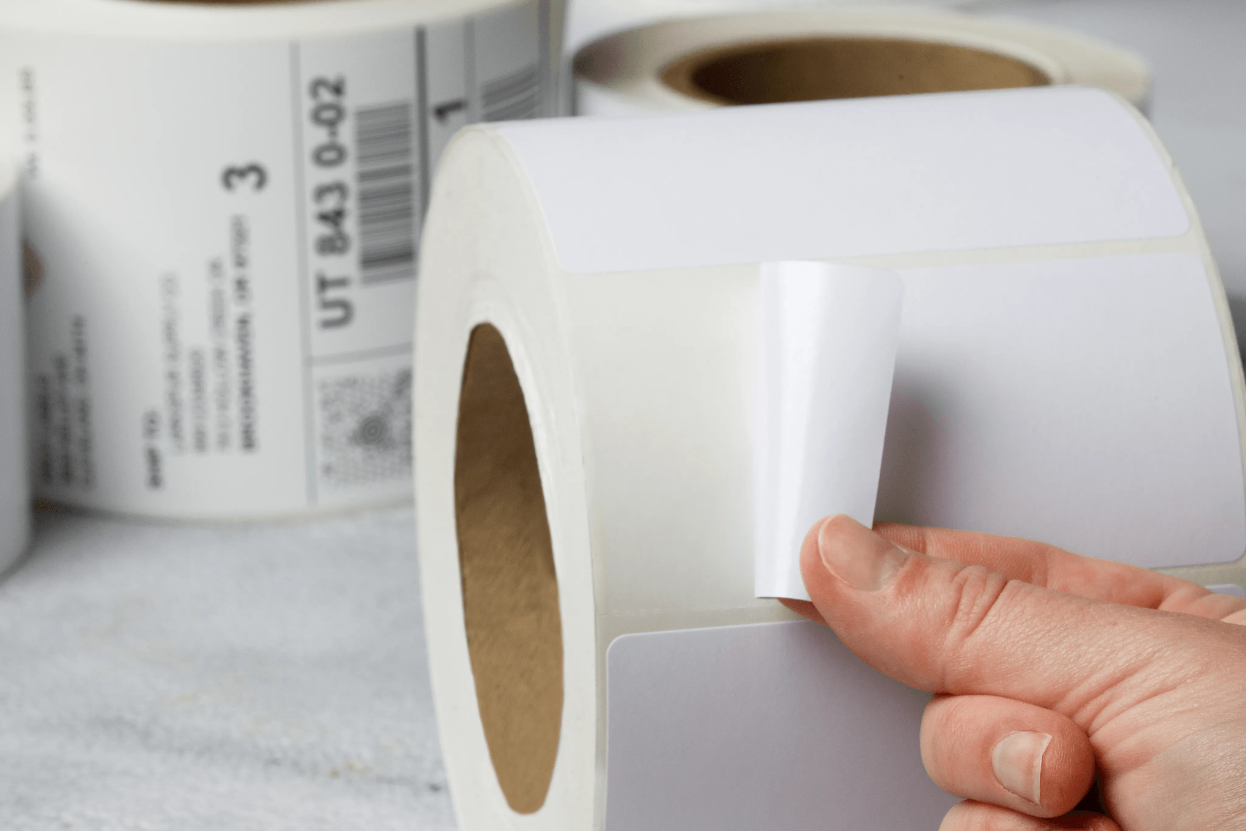 hand holding a white thermal label roll with shipping information visible