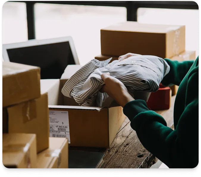 a person packing a folded shirt into a cardboard box