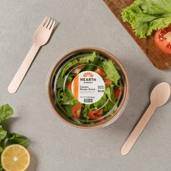 Fresh salad bowl with circular branded label on wooden table