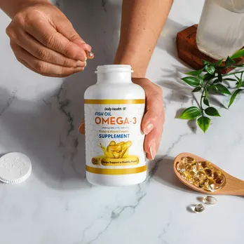 Hand applying orange supplement label to clear bottle with yellow capsules visible inside