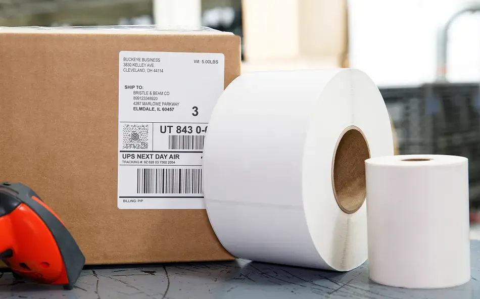 2 rolls of thermal labels next to a cardboard box with a shipping label